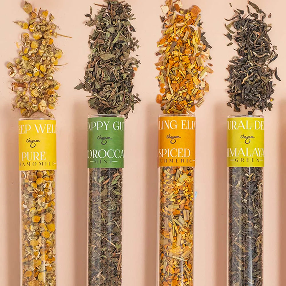 Four tubes of different types of tea (chamomile, mint, turmeric, himalayan green) with visible labels on a pink background