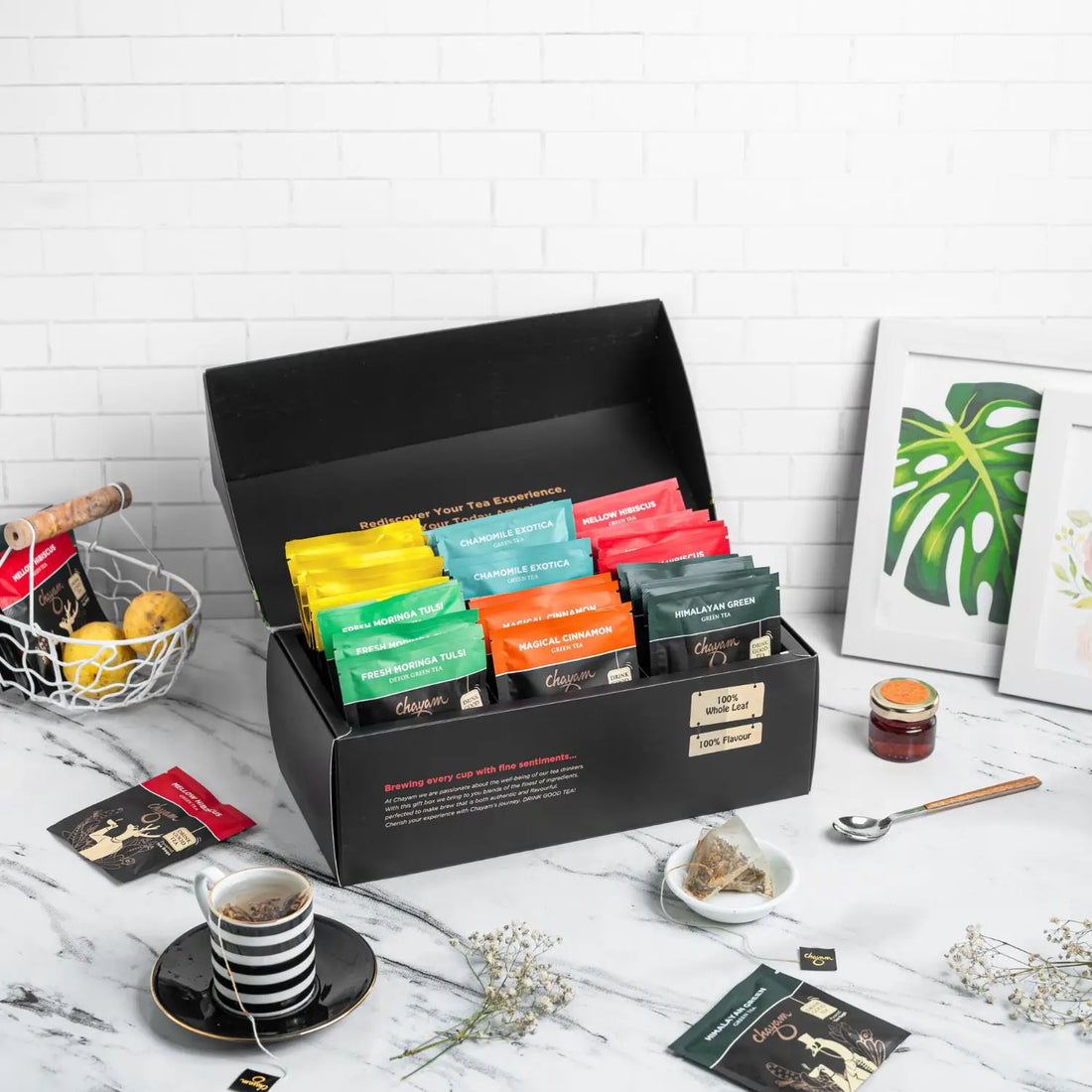 Collection of tea bags in a black display box on a marble surface with a white brick wall background.