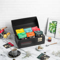 Collection of tea bags in a black display box on a marble surface with a white brick wall background.